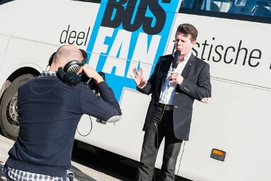Tony presenteert voor een bus en wordt gefilmd, zoals een nieuwsanker